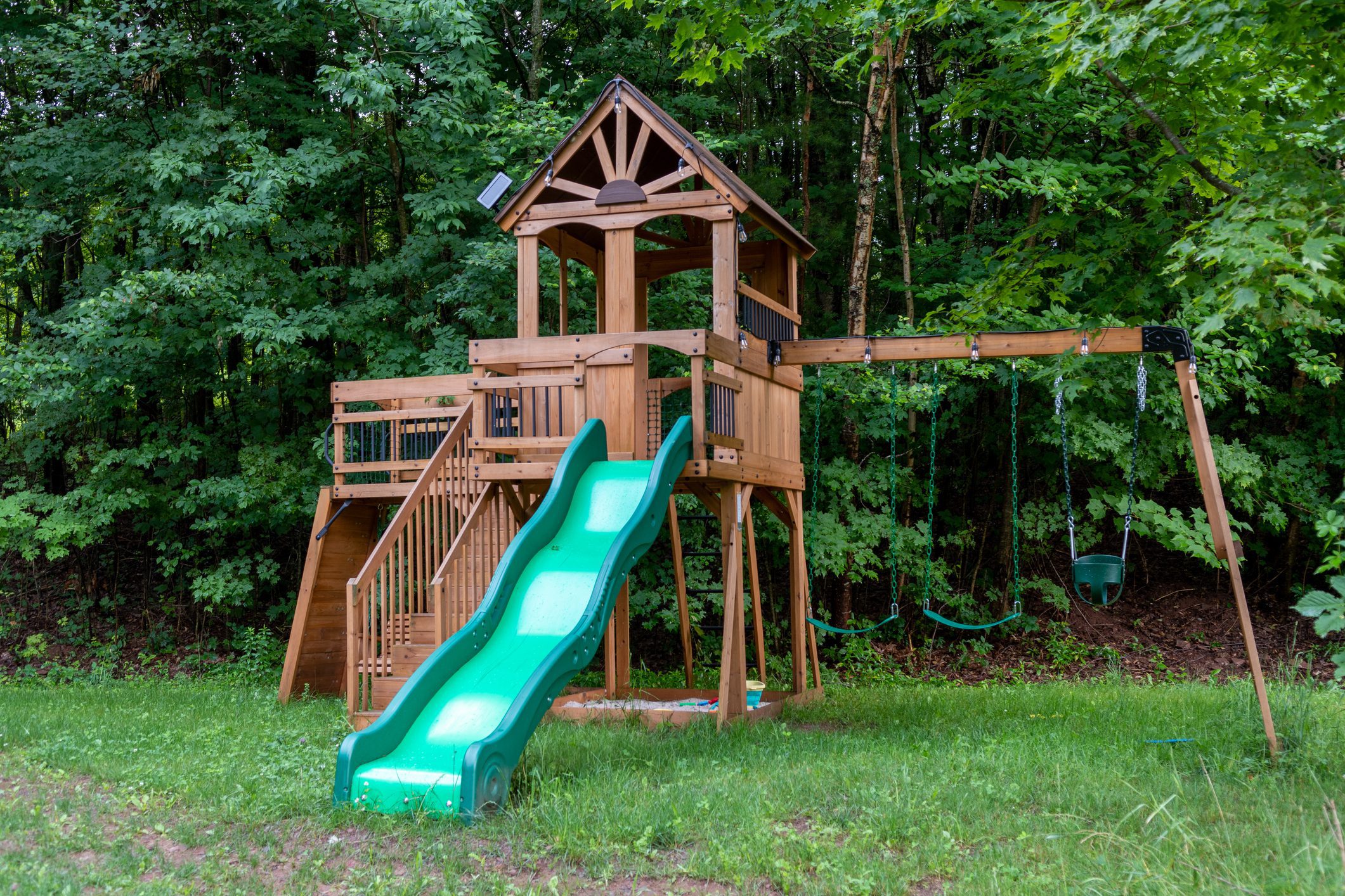 Wooden backyard playset with green slide, swings